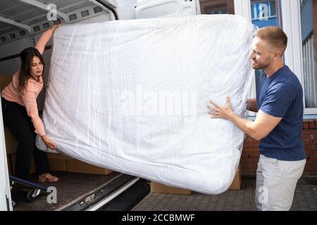 Paar Entladen Matratze Aus Van Oder Lkw Während Umzug Haus Im Freien Stockfoto