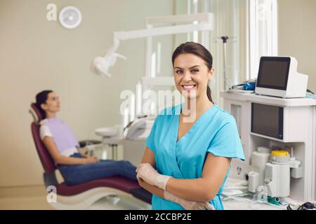 Lächelnder Zahnarzt steht und schaut mit sitzendem Patienten auf die Kamera Im Hintergrund Stockfoto