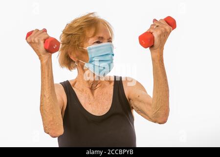 Ältere Frau, die mit Hanteln belastet ist, während sie ein Gesicht trägt Maske Während Der Corona Virus Epidemie Stockfoto