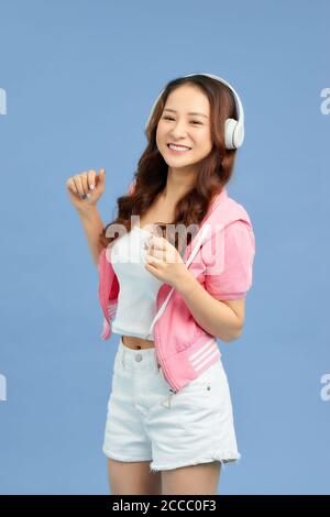 Attraktive junge asiatische Frau, die Musik hört und auf blauem Hintergrund tanzt. Stockfoto