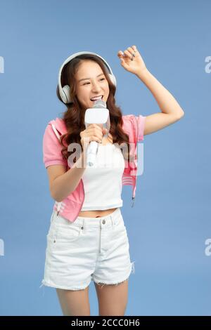 Schöne asiatische Mädchen mit Mikrofon singt und Kopfhörer isoliert auf blauem Hintergrund. Stockfoto