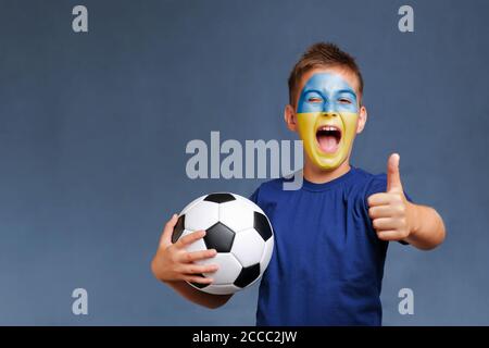 Schöner schreiender ukrainischer Fanboy hält Fußball und zeigt Daumen Nach oben Stockfoto