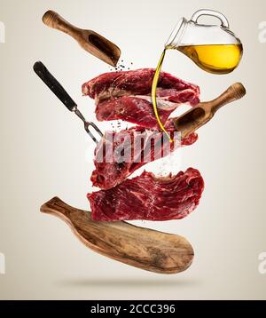 Stücke von rohen Steaks mit Zutaten zum Kochen, fliegen serviert auf Woodenboard. Konzept der Zubereitung von Speisen in geringer Schwerkraft-Modus. Getrennt auf glatten Stockfoto