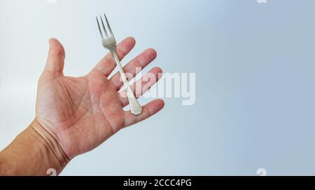 Kleine Stahlgabel in der Handfläche des Menschen, isoliert auf weißem Hintergrund. Kopierraum Stockfoto