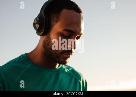 Porträt eines afroamerikanischen Athleten mit kabellosen Kopfhörern. Nahaufnahme eines Fitnessmanns, der im Freien steht und Musik hört. Stockfoto