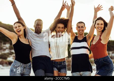 Fröhliche Gruppe von Freunden genießen ihren Urlaub. Multiethnische Freunde, die mit aufgehobenen Armen zusammen stehen und Spaß haben. Stockfoto