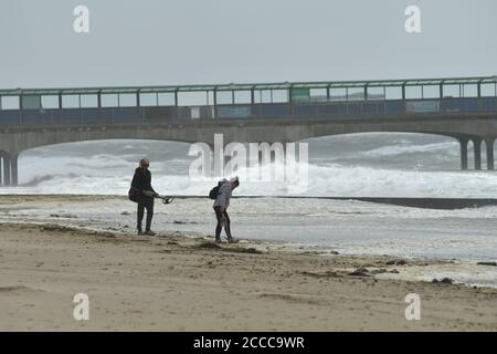 Sturm Ellen schlägt die Südküste von England auf dem Höhepunkt der Sommerferiensaison mit Windböen von bis zu 60 mph und einer Flut. Ein Paar mit einem Metalldetektor durchkämmt den windigen Strand, Boscombe, Bournemouth, Dorset, Großbritannien, 21. August 2020 Stockfoto