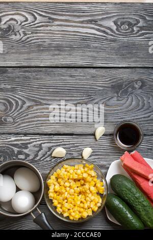 Krabbenstäbchen, Hühnereier und Gemüse für die Salatzubereitung. Sie liegen auf bemalten Kiefernbrettern. Von oben. Stockfoto