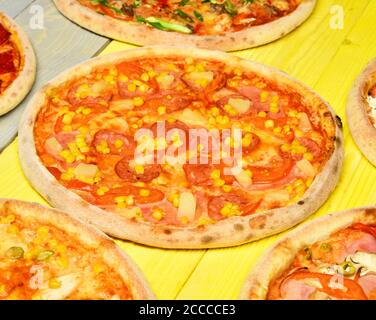 Pepperoni oder Hawaii Pizza mit Ananasstückchen. Pizza mit Speck, Pfefferoni, Tomaten und Mais auf gelbem Holzhintergrund. Fast Food und italienische Küche Konzept. Nehmen Sie Lebensmittel mit knackigen Kanten. Stockfoto