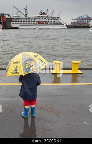 Hamburg, Deutschland. August 2020. Mit einem gelben Regenschirm schützt sich ein junger Mann im Hamburger Hafen vor dem Regen. Nach vielen trockenen, sonnigen Tagen regnet es wieder in der Hansestadt. Quelle: Ulrich Perrey/dpa - ACHTUNG: Nur zur redaktionellen Verwendung im Zusammenhang mit der aktuellen Berichterstattung und nur bei vollständiger Erwähnung der oben genannten Credit/dpa/Alamy Live News Stockfoto