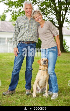 Ein glückliches Paar Senioren mit Haus und Hund steht da Der Garten Stockfoto