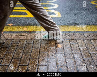 Mans Beine und Füße zu Fuß durch den Bürgersteig auf einem Regentag Stockfoto