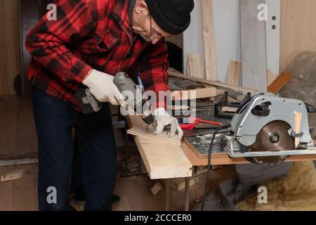 Der ältere Mann arbeitet als Zimmermann in der Werkstatt. Aktives Alter Stockfoto