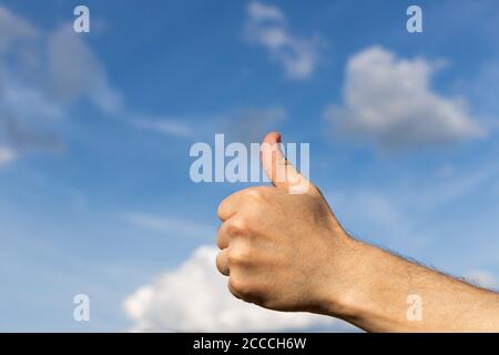 Die Hand des Mannes zeigt ein Schild mit den Daumen nach oben auf dem blauen Himmel Stockfoto