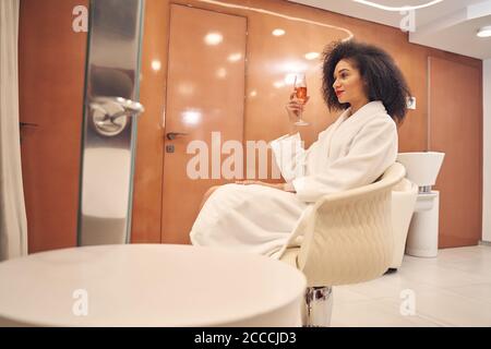 Junge bewundernswerte Dame genießen Champagner im Salon Stockfoto