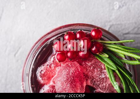 Frischer eisgekühlter Fruchtcocktail im Glas, erfrischender Sommerdrink mit roter Johannisbeere mit Rosmarinblatt auf Steinbeton-Hintergrund, Makroansicht von oben Stockfoto