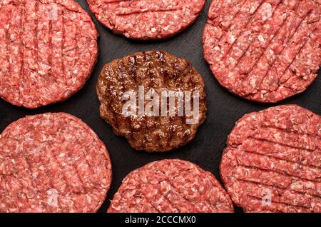 Oben mit Burger Beef Patties isoliert auf einem schwarzen Tisch. Flache Laie mit gekochten und ungekochten Burger-Patties. Hamburger Beef Patty gegrillt, top vie Stockfoto