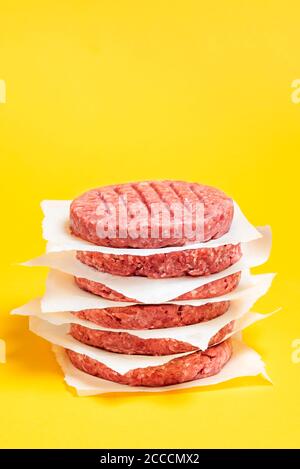 Beef Patties gestapelt mit Papier zwischen ihnen auf einem gelben Hintergrund. Hamburger rohes Fleisch wird zum Kochen zubereitet. Stockfoto