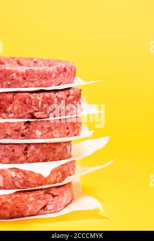 Nahaufnahme mit einem Stapel Burger-Patties vor einem gelben Hintergrund. Rohe Beef Burger Patties übereinander auf einem gelben Tisch. Stockfoto
