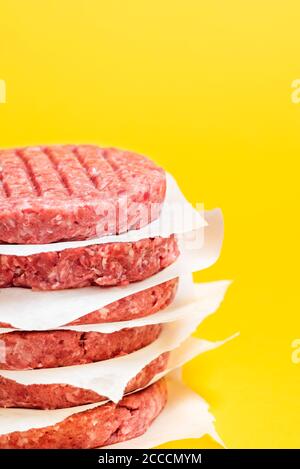 Stapel von rohen Rindfleisch Hamburger Patties mit Papier zwischen ihnen vor einem gelben Hintergrund. Für den Grill zubereitetes, ungekohltes Hackfleisch. Stockfoto