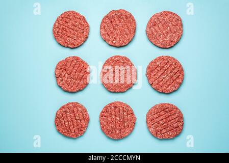 Oben mit rohen Beef Patties für Burger, symmetrisch auf blauem Hintergrund angeordnet. Flach legen mit neun ungekochten Burger-Patties isolieren Stockfoto