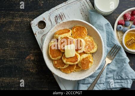 Pfannkuchen, Müsli, winzig dünne, lustige Krümel, Kinderessen. Frühstück mit Getränk, dunkler Tisch Stockfoto