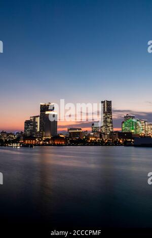 Minato Mirai Skyline während des Sonnenuntergangs mit der Reflexion im Meer. Langzeitbelichtung. Stockfoto