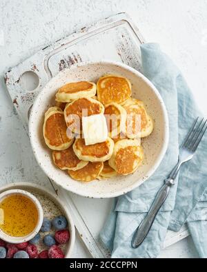 Pfannkuchen, Müsli, winzig dünne, lustige Krümel, Kinderessen. Frühstück mit Getränk, weißer Tisch Stockfoto