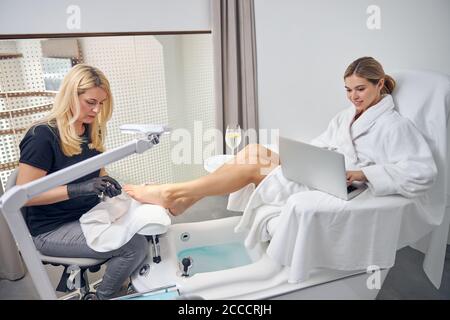 Fröhliche junge Frau mit Laptop im Spa-Salon Stockfoto