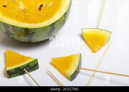 Stücke von gelber Wassermelone auf Stöcken. Platte auf einer weißen Oberfläche. Stockfoto