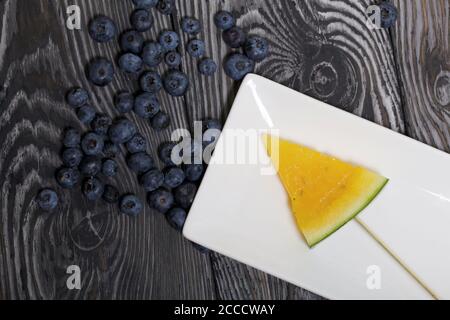 Stücke von gelber Wassermelone auf Spieße. Auf einen Teller legen. Platte auf bemalten Kiefernbrettern. Stockfoto