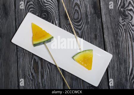 Stücke von gelber Wassermelone auf Spieße. Auf einen Teller legen. Platte auf bemalten Kiefernbrettern. Stockfoto