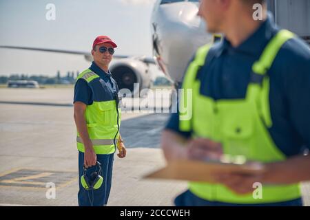 Flughafenmitarbeiter in Sonnenbrillen, die am Flugplatz stehen Stockfoto