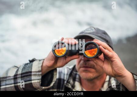 Nahaufnahme eines Mannes, der durch ein Fernglas blickt und dabei kein sichtbares Gesicht hat. Stockfoto