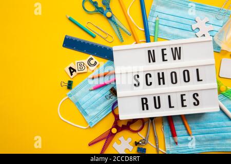 Neue Schulregel-Botschaft mit Schulausrüstung und Covid-Masken Stockfoto