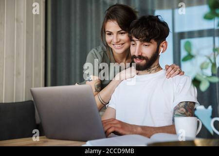 Schönes lächelndes junges Paar mit Laptop-Computer, während die Zeit in der Küche, Kaffee trinken Stockfoto