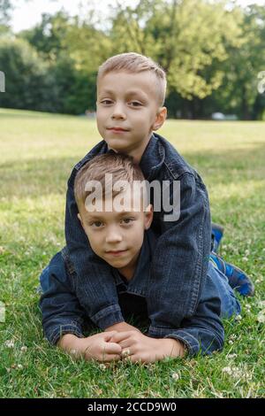 Zwei Jungen von drei Jahren in Jeans liegen auf dem Gras und umarmen sich. Zwei enge Freunde, zwei Cousins. Familienbeziehungen zwischen Brüdern Stockfoto