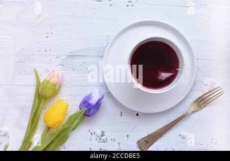 Frische blaue Tulpe und Tasse roten Kräutertee / Frau Gießt heißen roten Tee in einer Tasse auf einem weißen Holztisch Stockfoto