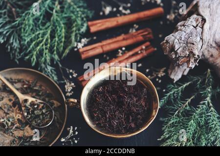 Goldene Teetase gefüllt mit Schmutz auf Wiccan Hexenaltar. Zauberguss Zutaten - Zimtstangen, schwarze Erde, getrocknete Kräuter, immergrüne Tannenzweige Stockfoto