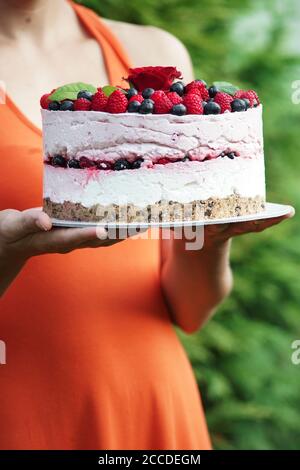 Junge Frau im Garten hält einen Himbeer-Käsekuchen Stockfoto