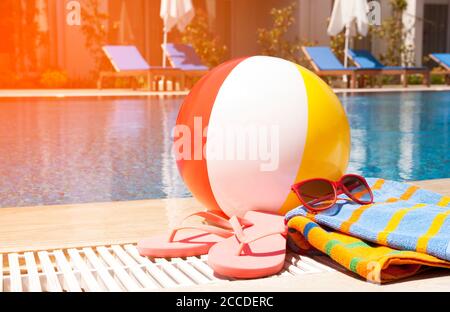 Strandball, Handtuch, Sonnenbrille und Flip-Flops neben dem Pool. Stockfoto