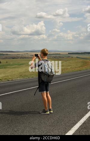 Ein junger Mann macht als nächstes Bilder auf einer Telefonlandschaft Zu einer Landstraße Stockfoto