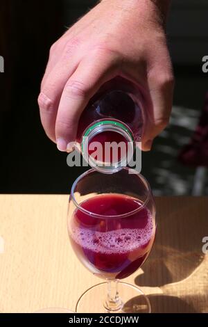 Nahaufnahme Hand Gießen aus roten Fruchtsaft oder Granatapfelsaft In einer Flasche in ein Glas auf einem Holztisch Stockfoto