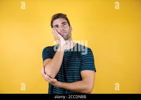 Junger gutaussehender Mann Denken konzentrierte sich auf Zweifel mit dem Finger auf Kinn und Blick nach oben wundernd Stockfoto
