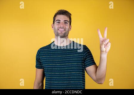 Jungen gutaussehenden Mann legere blaues T-Shirt über gelb isoliert Hintergrund lächelnd mit glücklichen Gesicht in die Kamera winking tun Sieg unterzeichnen. Anzahl Stockfoto