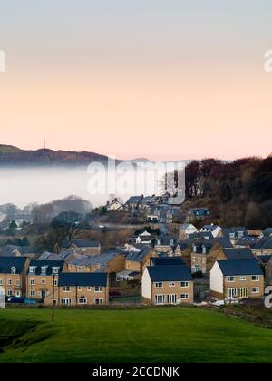 Neue Häuser am Stadtrand von Buxton im Derbyshire Peak District mit Nebel auf den Hügeln im Hintergrund. Stockfoto