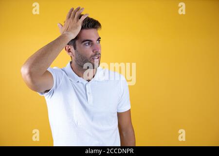 Junger gutaussehender Mann, der eine Hand auf ihren Kopf legte, sorgte sich, als hätte er etwas vergessen, das auf rosa Hintergrund stand. Stockfoto