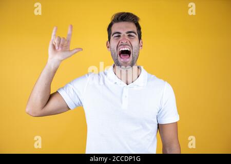 Junger schöner Mann trägt lässige T-Shirt über gelb isoliert Hintergrund schreien mit verrückten Ausdruck Rock-Symbol mit Händen nach oben tun. Musikstar. Stockfoto
