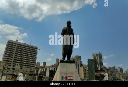 Beirut, Libanon. August 2020. Eine Statue eines libanesischen Immigranten steht vor schwer beschädigten Gebäuden in der Nähe des Ortes der massiven Hafenexplosion am 4. August. Mehr als zwei Wochen nach der Explosion, die die libanesische Hauptstadt erschütterte, begannen einige Bewohner nach Hause zurückzukehren, um zu säubern, zu reparieren und zu versuchen, wieder in ihr normales Leben zurückzukehren. Quelle: Marwan Naamani/dpa/Alamy Live News Stockfoto