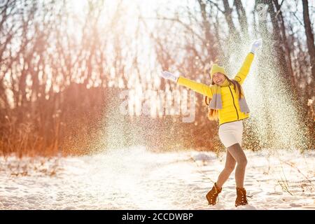 Winter Schnee Spaß Frau spielen Schneewerfen feiern kaltes Wetter. Mädchen in gelben Oberbekleidung Handschuhe, Stiefel, Hut, Schal, Mantel, genießen im Freien in Stockfoto